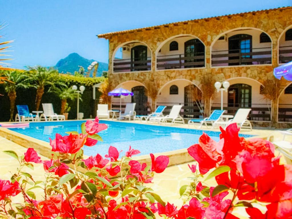 a resort with a swimming pool and red flowers at VELINN Pousada Casa de Pedra Ilhabela in Ilhabela