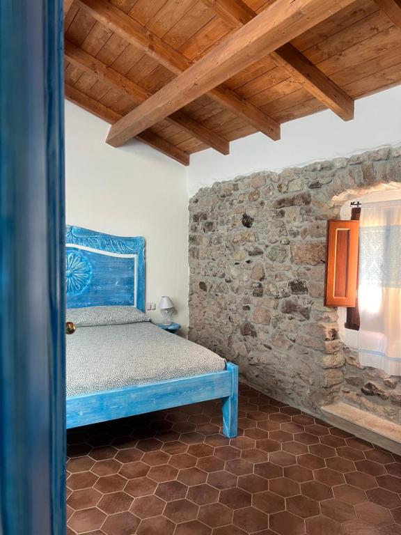 a bedroom with a blue bed and a stone wall at Regnos Altos boutique rooms in Bosa