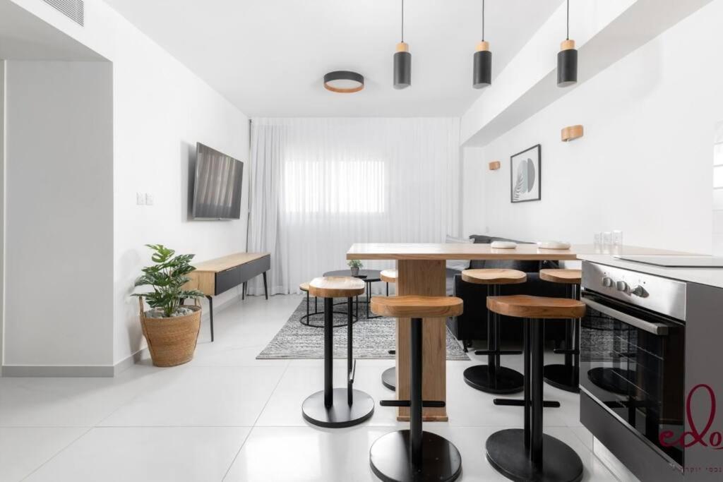 a white kitchen with a table and stools at דירה משפחתית מרווחת 50 מטר מהים - By Edom in Eilat