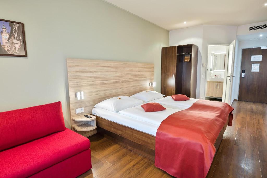 1 dormitorio con 1 cama grande y 1 sofá rojo en Austria Trend Hotel Salzburg Messe, en Salzburgo