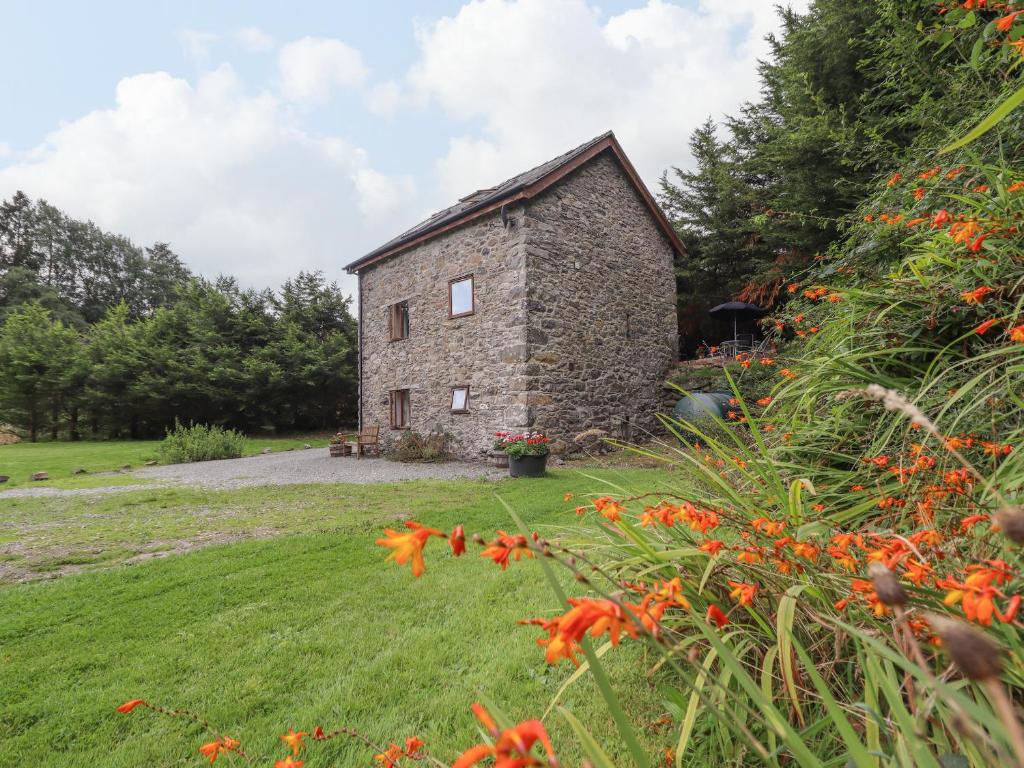 una vieja casa de piedra en un campo con flores en Yr Hen Felin, en Oswestry