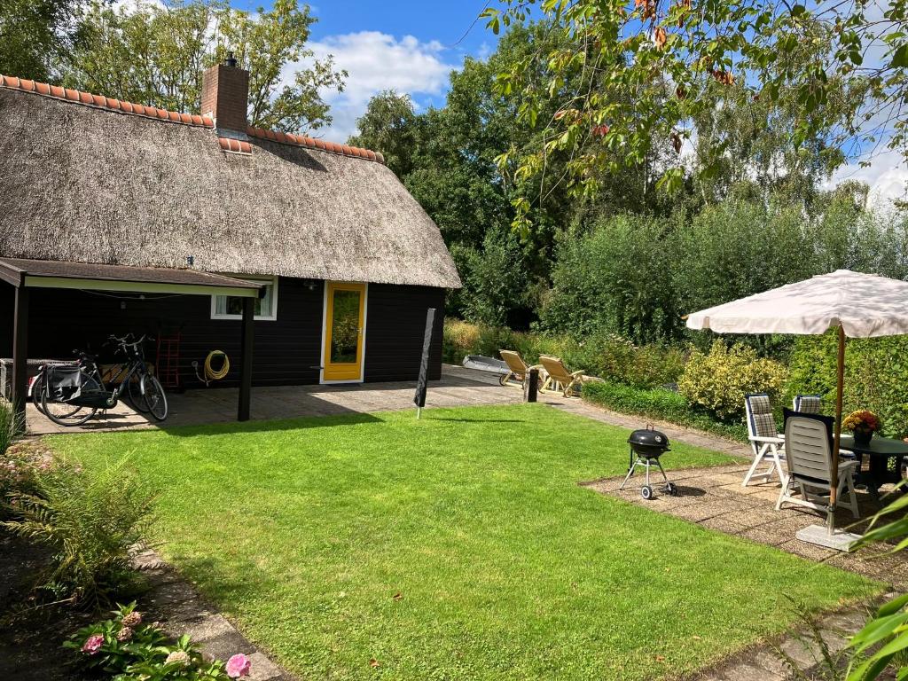 a house with a thatch roof with a grill and a grass yard at Oasis Giethoorn in Giethoorn