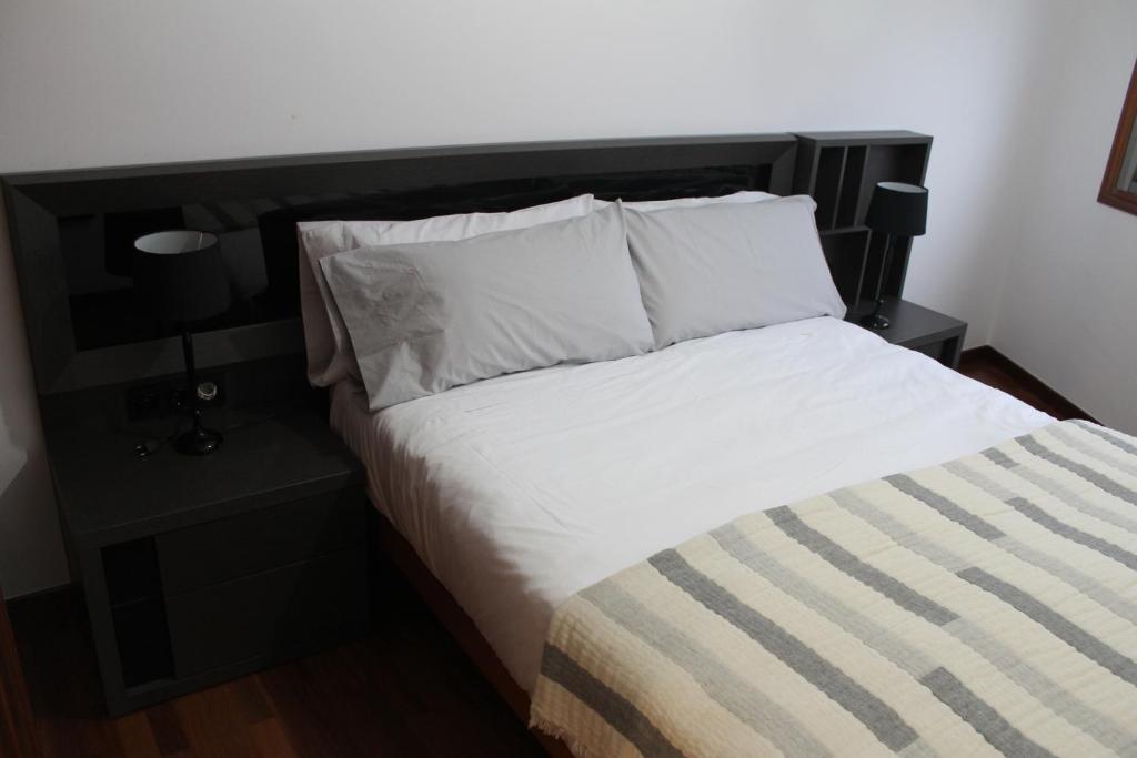 een bed met een zwart hoofdeinde en witte lakens en kussens bij CAMINO INGLES Habitación Luxe doble Baño y cocina in A Coruña