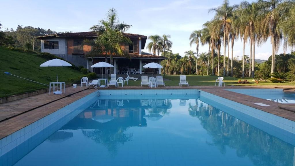 ein Pool mit Stühlen und ein Haus mit Palmen in der Unterkunft Fazenda Água Clara in Monte Alegre do Sul