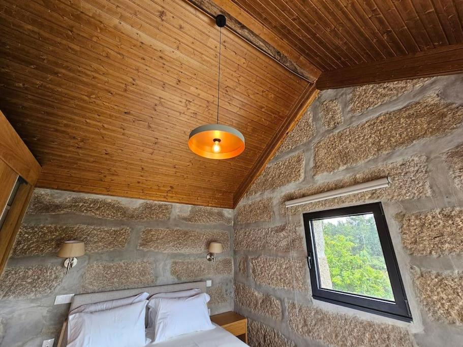 Dormitorio con paredes de piedra, cama y ventana en Quinta de Casal do Bairro Casa do Alpendre, en Guimarães