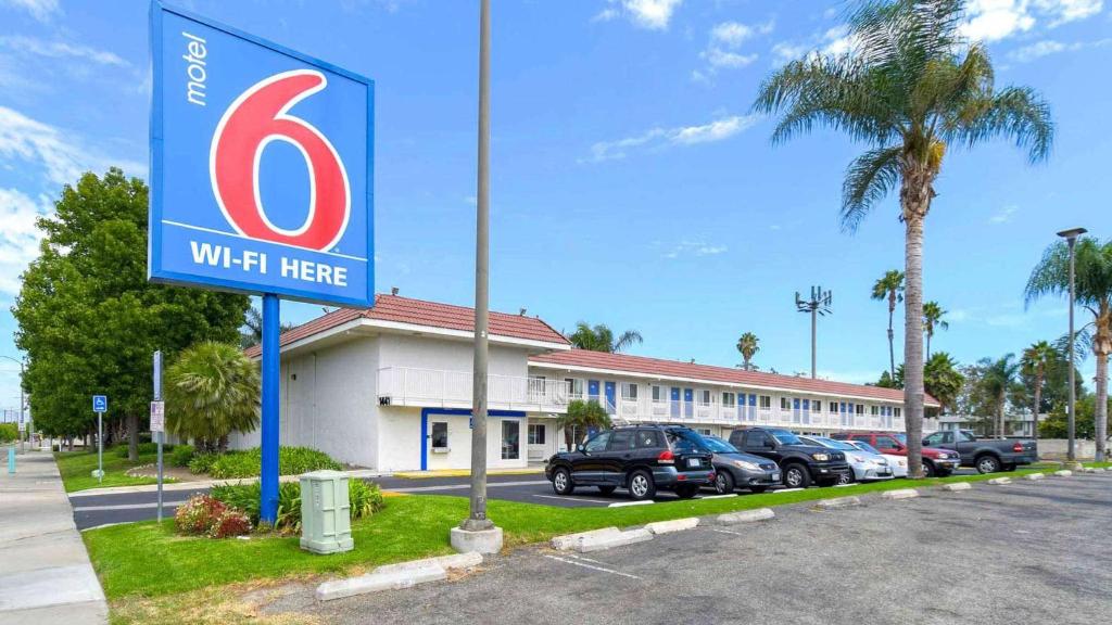 Una mujer aquí firma delante de un edificio en Motel 6-Costa Mesa, CA, en Costa Mesa