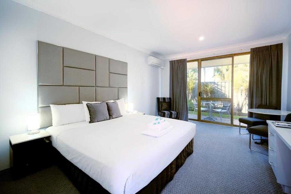 a hotel room with a large bed and a balcony at Island Palms Motor Inn in Forster