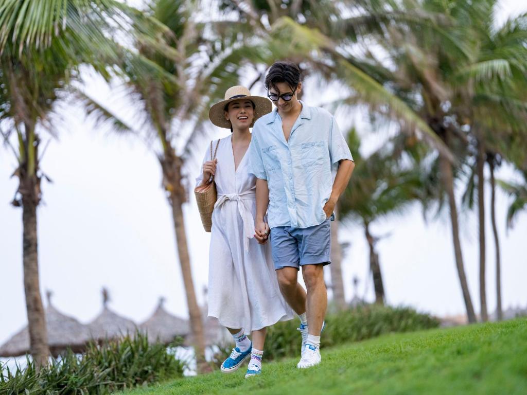 a woman and a man walking down a hill with palm trees at DLG Hotel Danang in Da Nang
