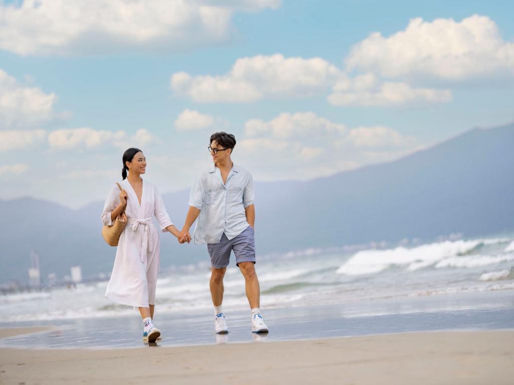 a man and a woman walking on the beach at DLG Hotel Danang in Da Nang