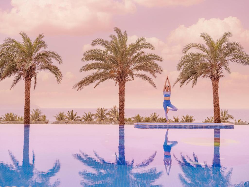 a woman doing yoga on the edge of a swimming pool with palm trees at DLG Hotel Danang in Danang