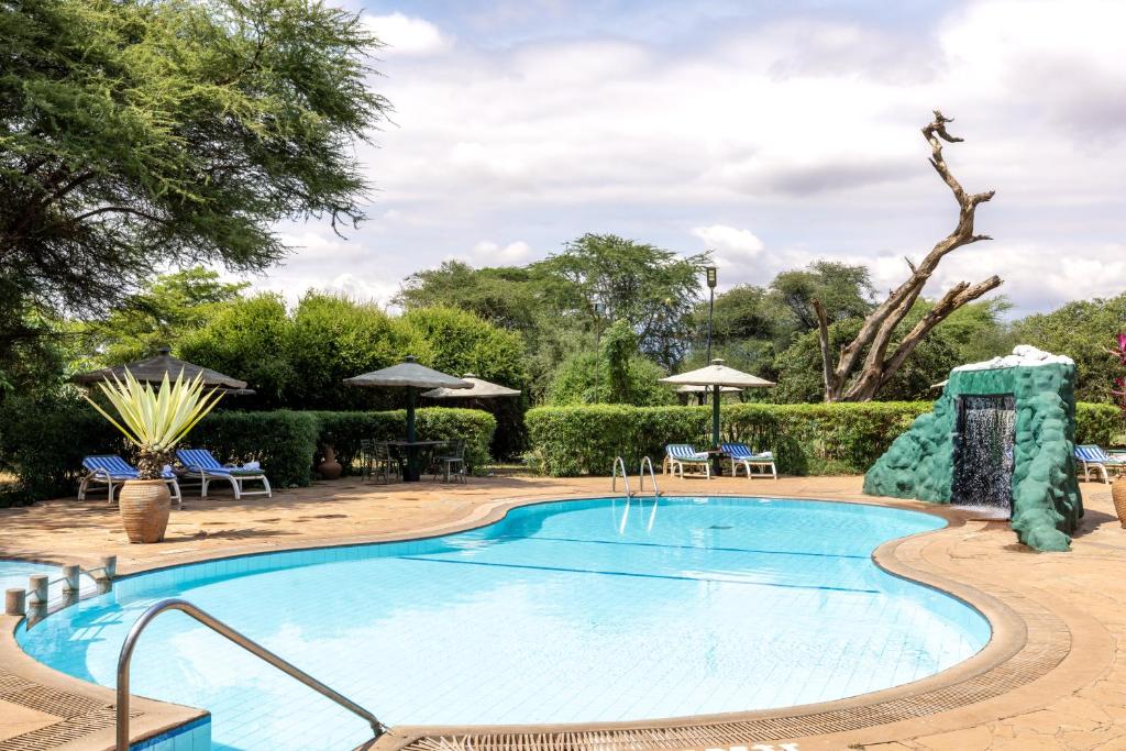 a pool at a resort with chairs and umbrellas at Sentrim Amboseli Lodge in Amboseli