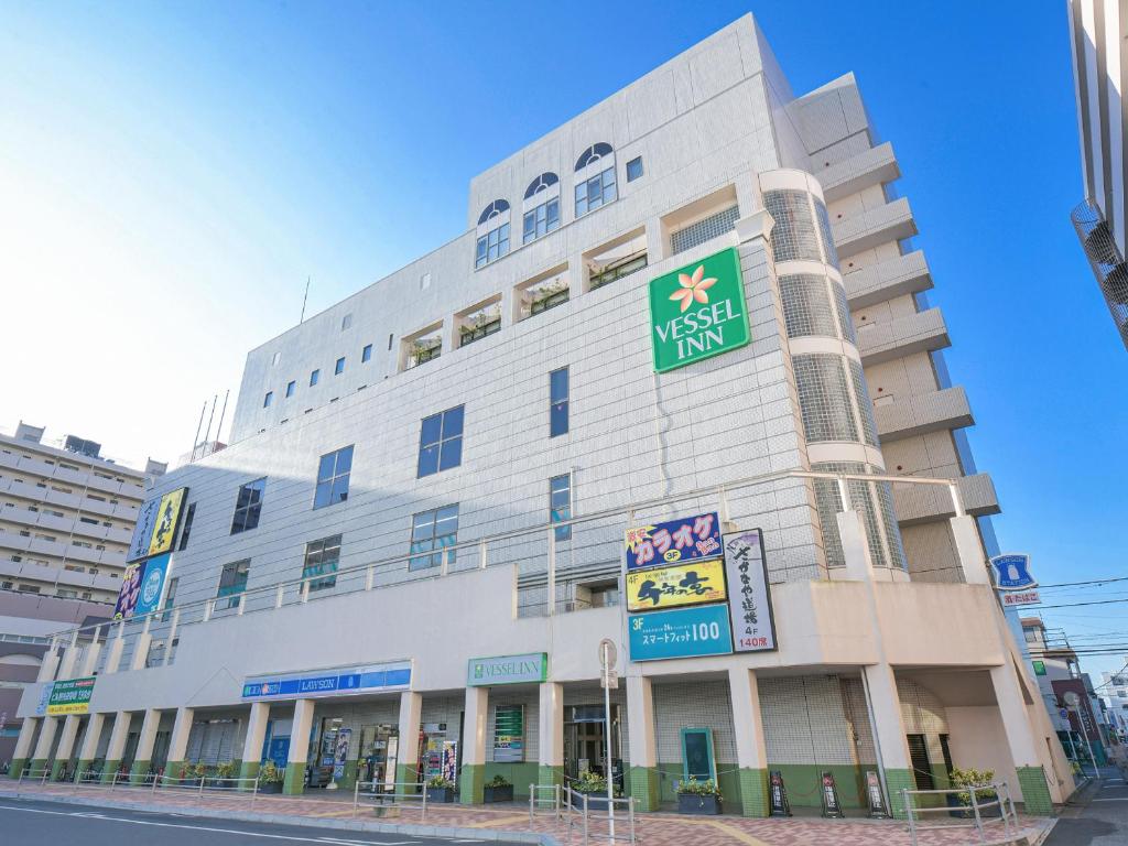 Un alto edificio bianco con un cartello sopra di Vessel Inn Yachiyo Katsudai Ekimae a Yachiyo