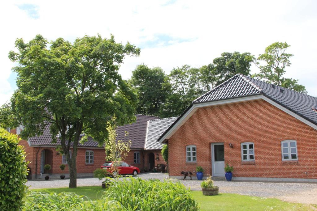 une maison en briques rouges avec un arbre dans la cour dans l'établissement Skelgaard Ferielejlighed, à Jelling