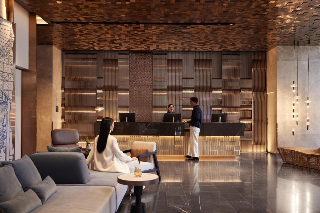 A contemporary reception lobby combines a long desk, lounge seating and floor-to-ceiling decorative lighting.