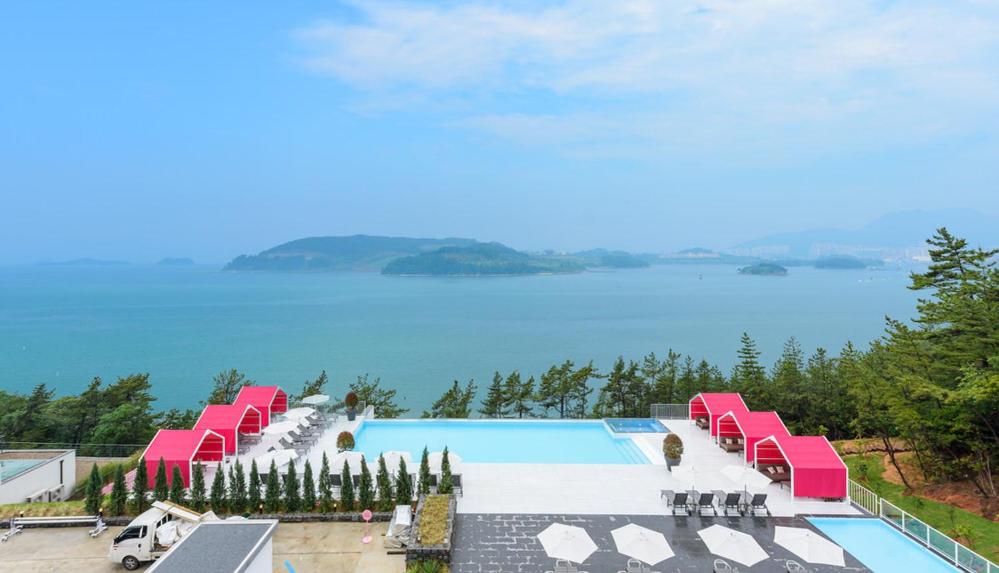 einen Pool mit rosa Stühlen und Blick auf das Wasser in der Unterkunft Vigo Resort in Yeosu