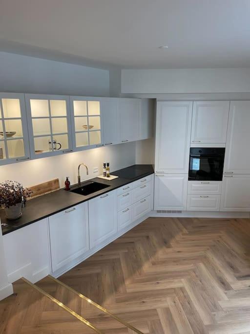 a kitchen with white cabinets and a wooden floor at Nyrenoveret charmerende lejlighed i Odense C! in Odense