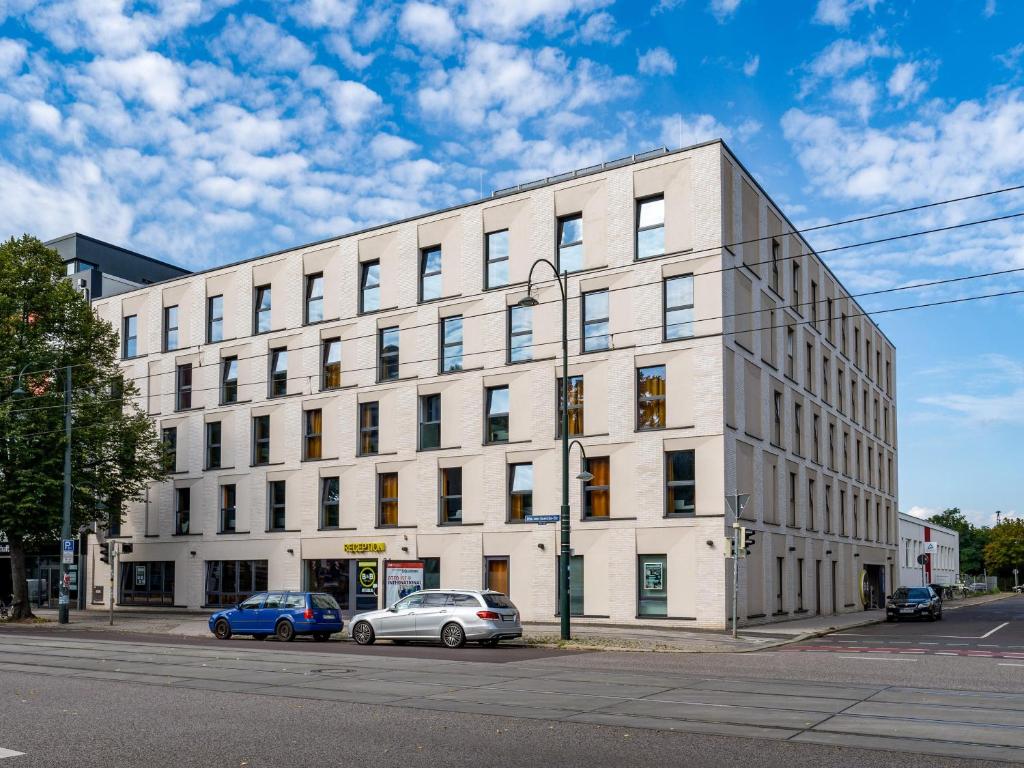un bâtiment blanc avec des voitures garées devant lui dans l'établissement B&B HOTEL Magdeburg-City, à Magdebourg