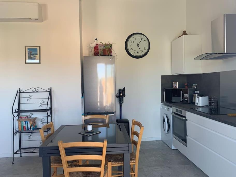 eine Küche mit einem Tisch und Stühlen sowie einer Uhr an der Wand in der Unterkunft Maison terrasse proche centre ville et ile de Ré in La Rochelle