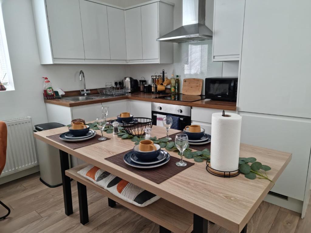 una cocina con una mesa de madera con platos y copas de vino en Central Watford Modern Apartment - Travellers & Contractors Welcomed, en Watford