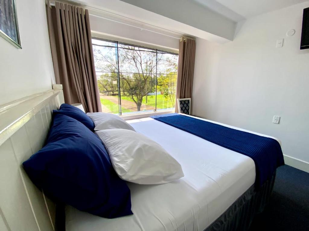 1 cama con almohadas azules y blancas y ventana en Hotel Renty Beach en Encarnación