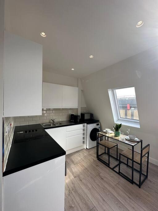 a kitchen with white cabinets and a black counter top at Modern flat in Victoria in London