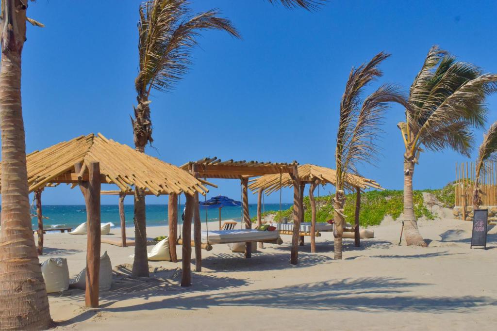 una playa con palmeras y sombrillas en la arena en Las Cabañas de Antica, en Vichayito