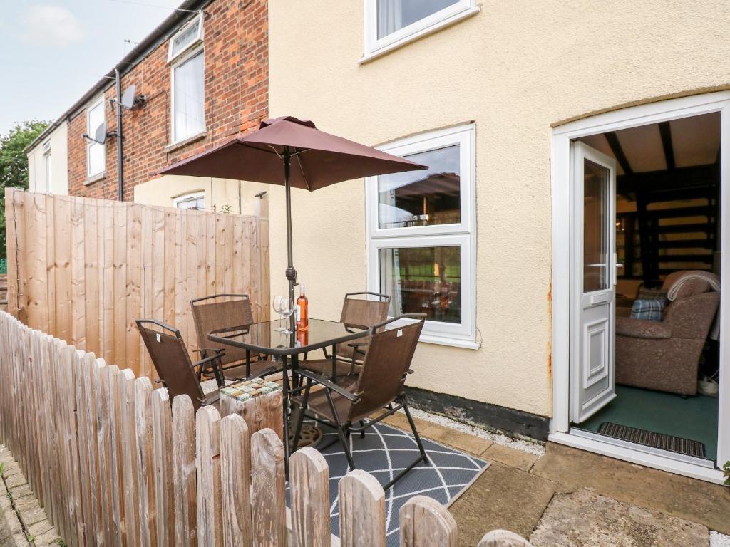 a patio with a table with an umbrella and a fence at Kathy's Cottage in King's Lynn