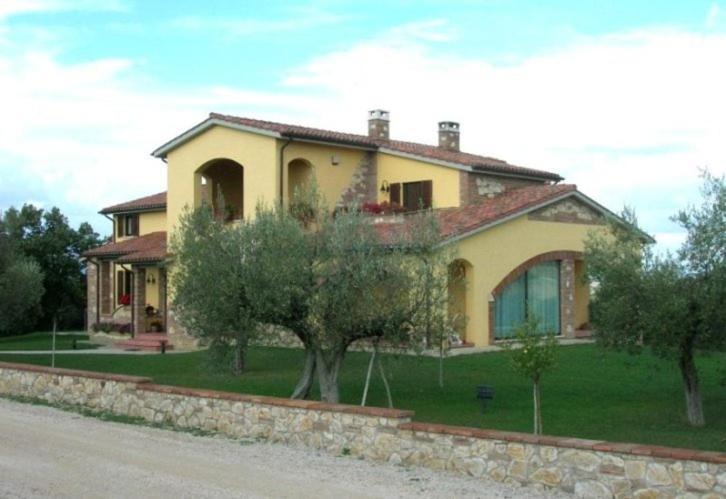 une grande maison jaune avec des arbres devant elle dans l'établissement B&B La Casa Fra Gli Olivi, à Marsciano