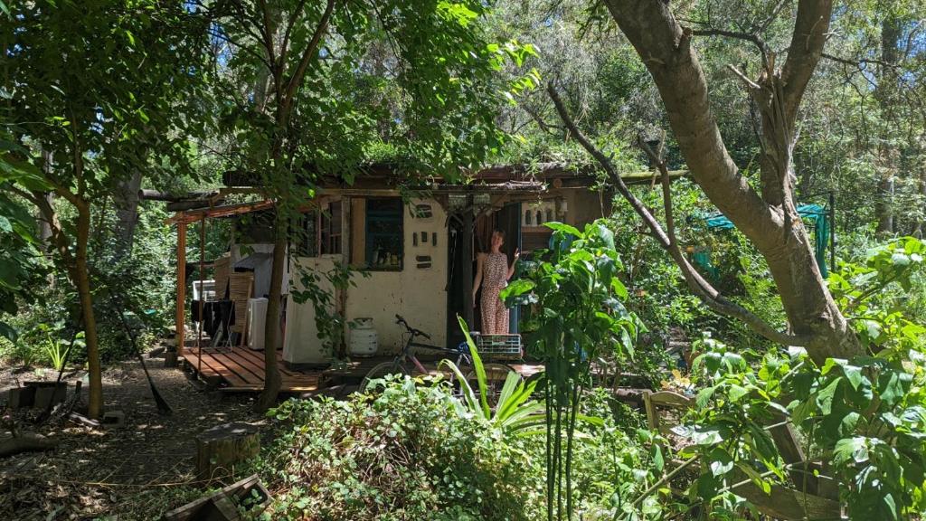 a woman standing in front of a house in the woods at Tiny home hexagonal de barro y techo vivo in Santa Ana