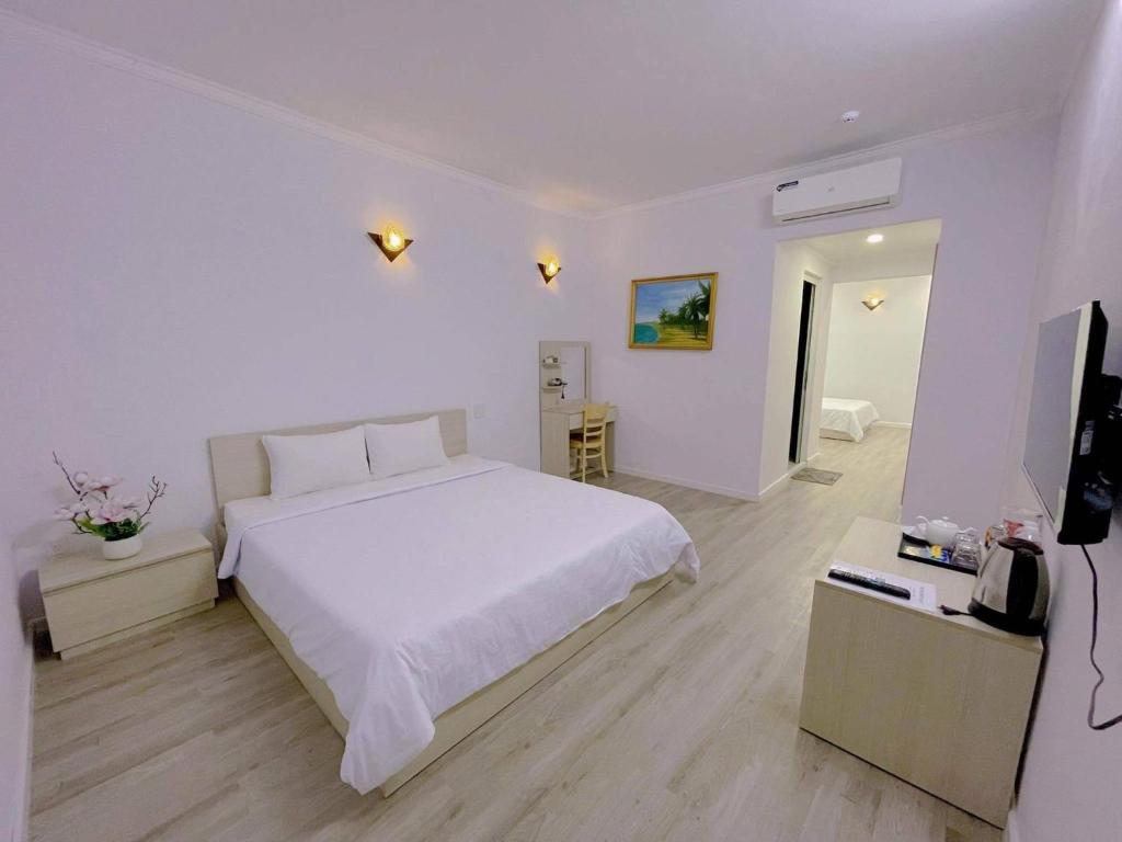 a white bedroom with a white bed and a television at Sai Gon Ha Tien Hotel in Hà Tiên