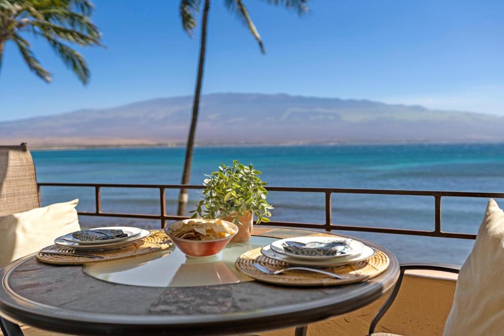 a table with plates of food on a balcony with the ocean at Island Sands 210 in Maalaea