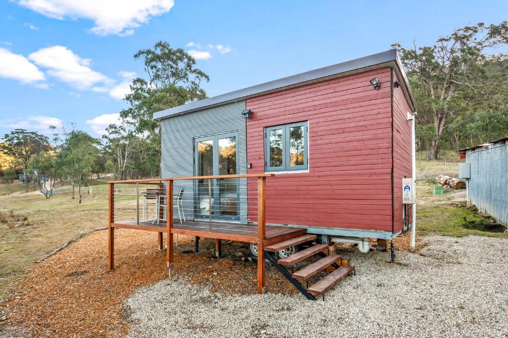 a red and grey tiny house with a deck at Tiny Home - Redbird in Hartley