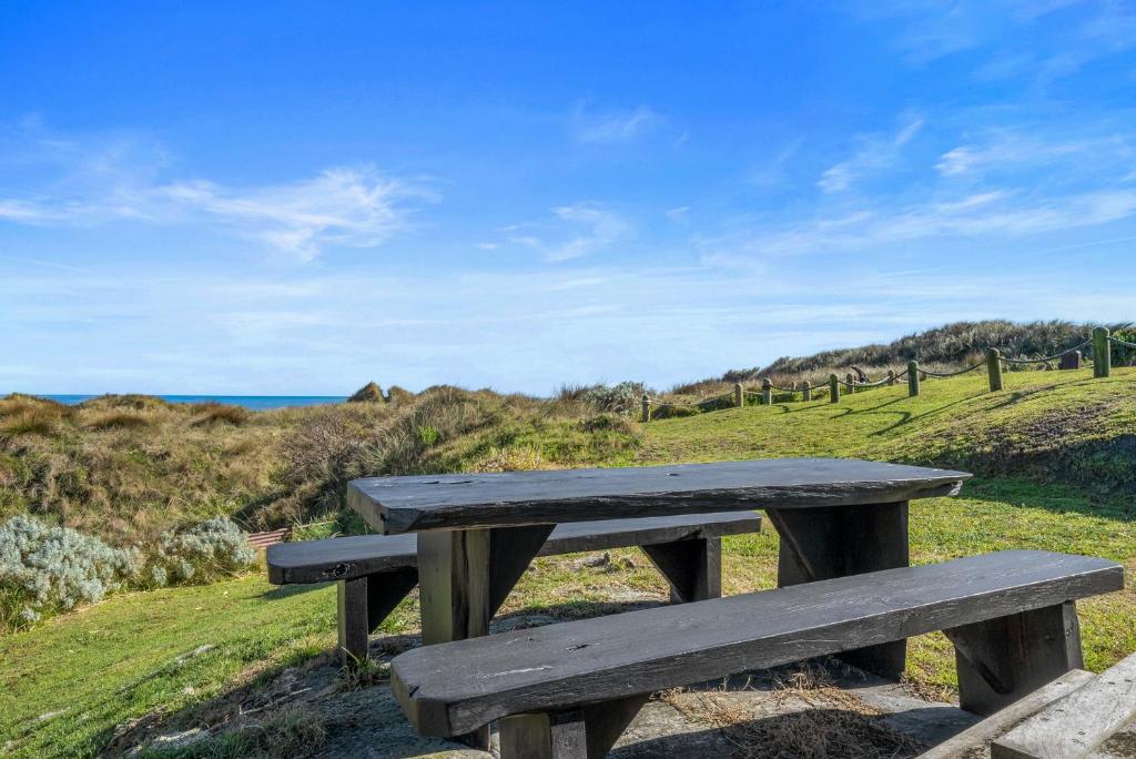 a wooden bench sitting on top of a hill near the ocean at Beachfront Favourite - Foxton Beach Holiday Home in Foxton Beach