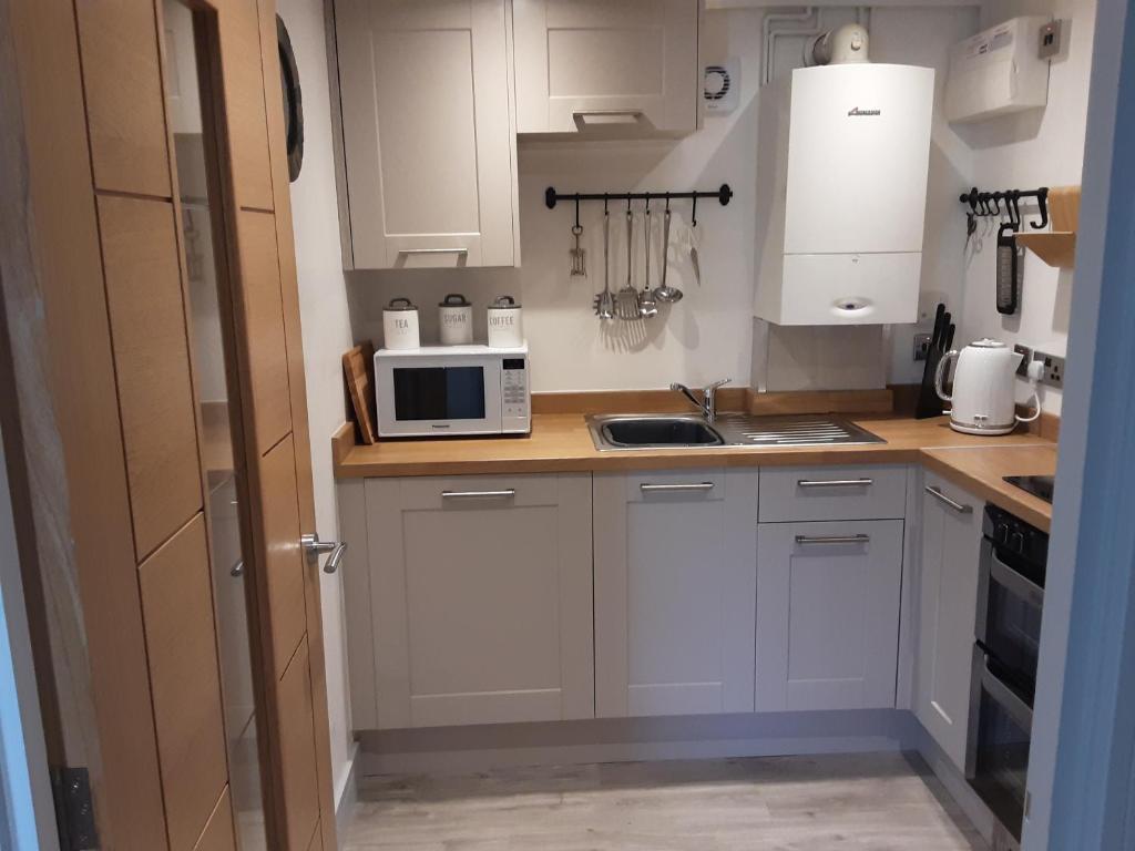 una pequeña cocina con armarios blancos y microondas en 2 The Maltings Apartments, en Shepton Mallet
