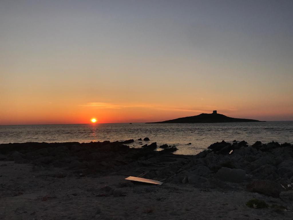 a sunset on the beach with a lighthouse in the distance at Summer House in Isola delle Femmine