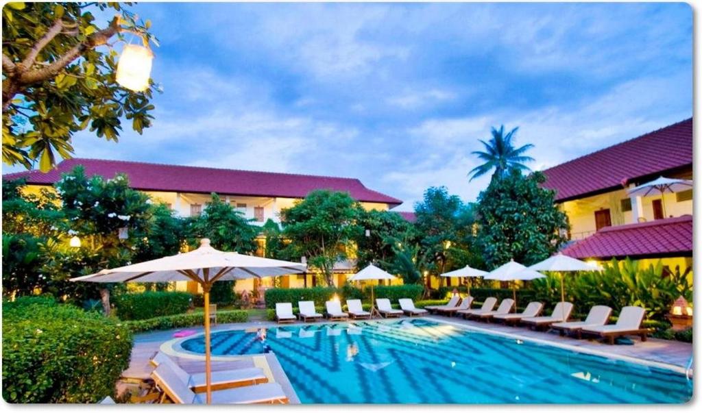 a pool with chairs and umbrellas and a hotel at Karinthip Village in Chiang Mai