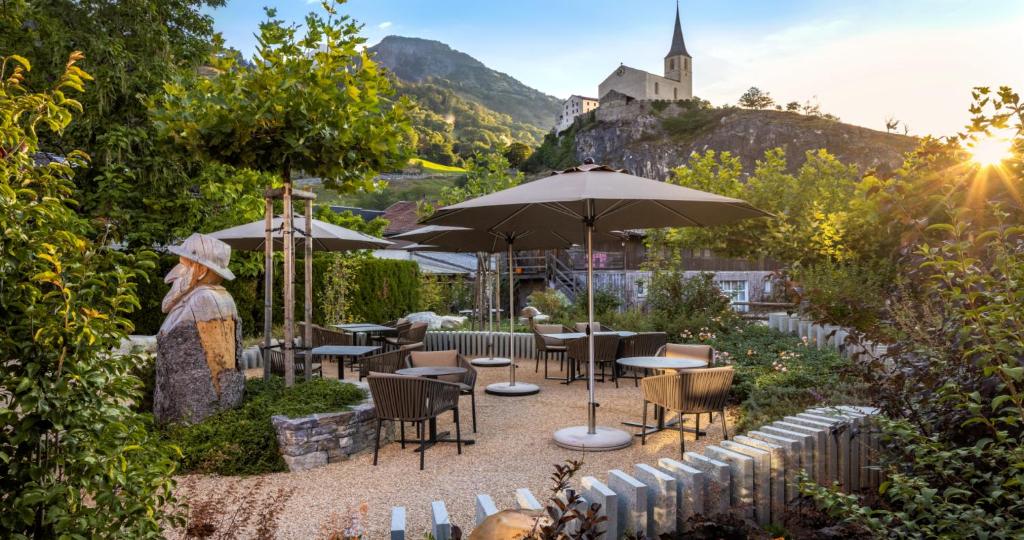 a patio with tables and umbrellas with a castle in the background at Kapitel 7 Boutique-Hotel in Raron