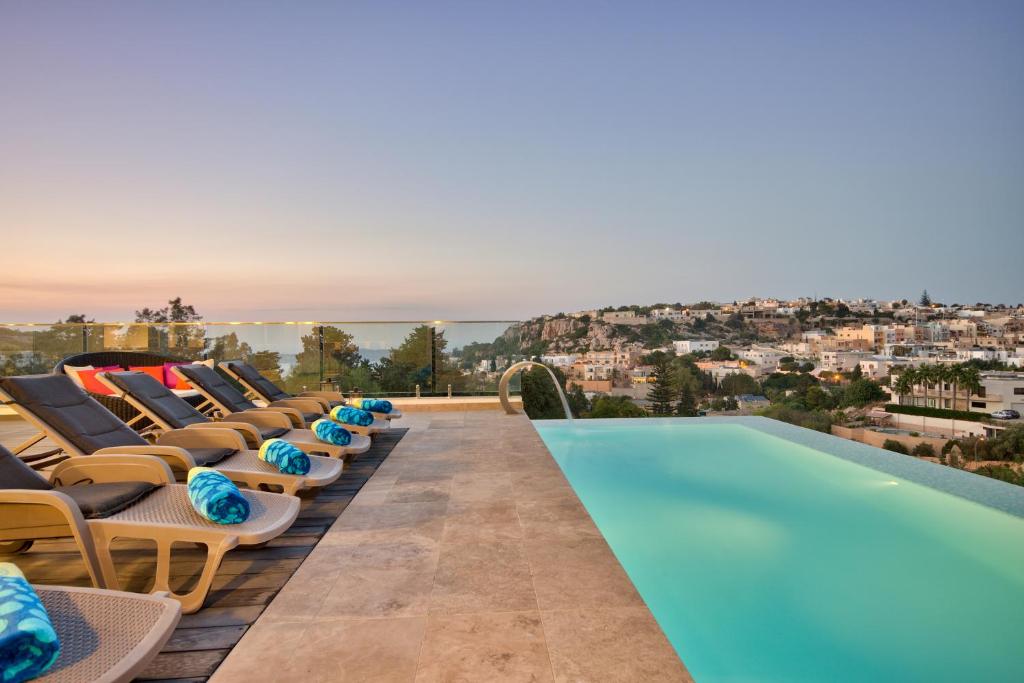 a row of lounge chairs next to a swimming pool at Villa Ghea - Indoor Jacuzzi Pool, Sauna and Games Room in Mellieħa