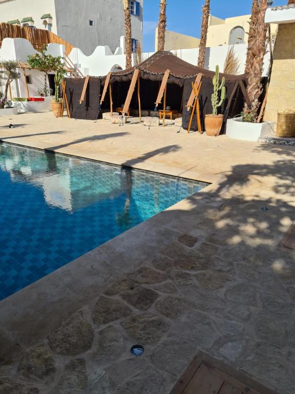 a swimming pool with blue water and palm trees at La Maison des Vagues in Sidi Kaouki