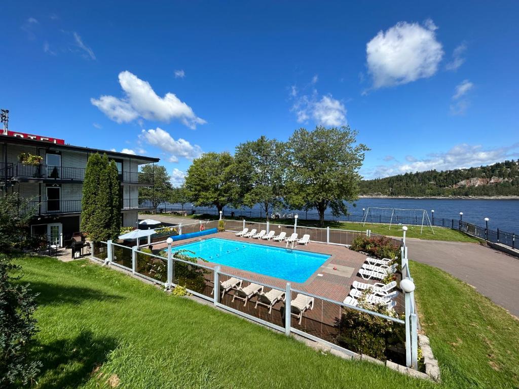 une piscine avec des chaises longues et un bâtiment dans l'établissement Motel Panoramique, à Saguenay