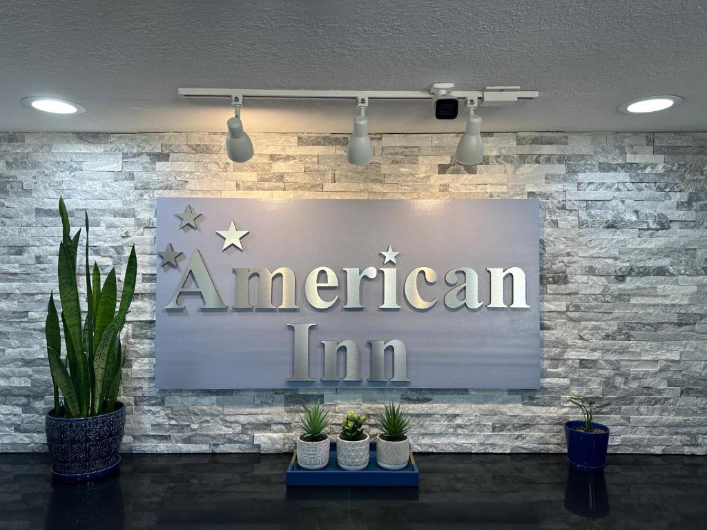 ein Schild eines amerikanischen Gasthofs an einer Ziegelwand mit Topfpflanzen in der Unterkunft American Inn Cedar Rapids South in Cedar Rapids