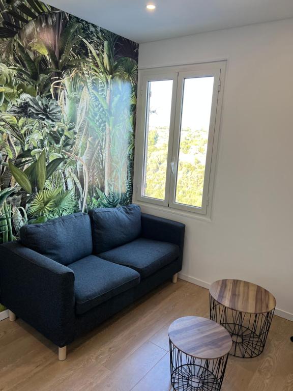 a living room with a blue couch and a tropical mural at Appartement Nice ouest au calme 10 minutes de la plage in Nice
