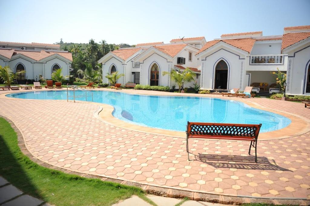 a swimming pool with a bench in front of a house at Riviera Hermitage Goa in Arpora