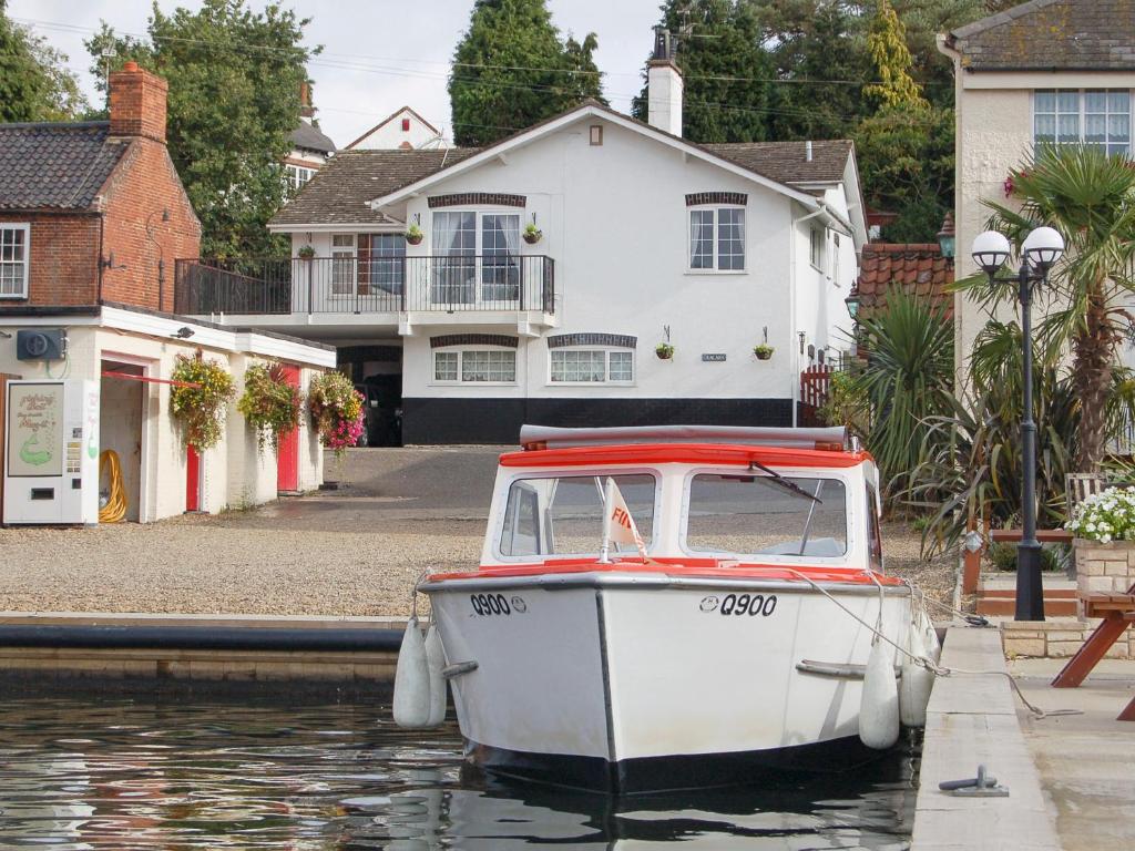 a small boat sitting in the water in front of a house at Tracara Cottage in Horning