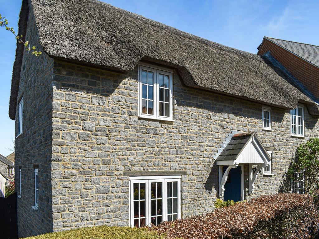 a stone house with white windows and a roof at Myrtle Cottage in Puncknowle