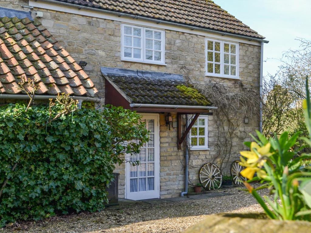 ein Steinhaus mit einer weißen Tür und Fenstern in der Unterkunft Keepers Cottage Annexe in Edith Weston