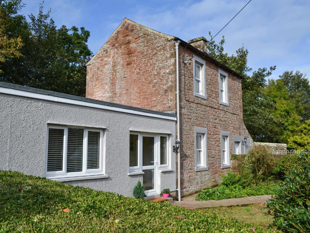 una antigua casa de ladrillo con ventanas blancas y un patio en Blaithwaite Cottage en Blencogo