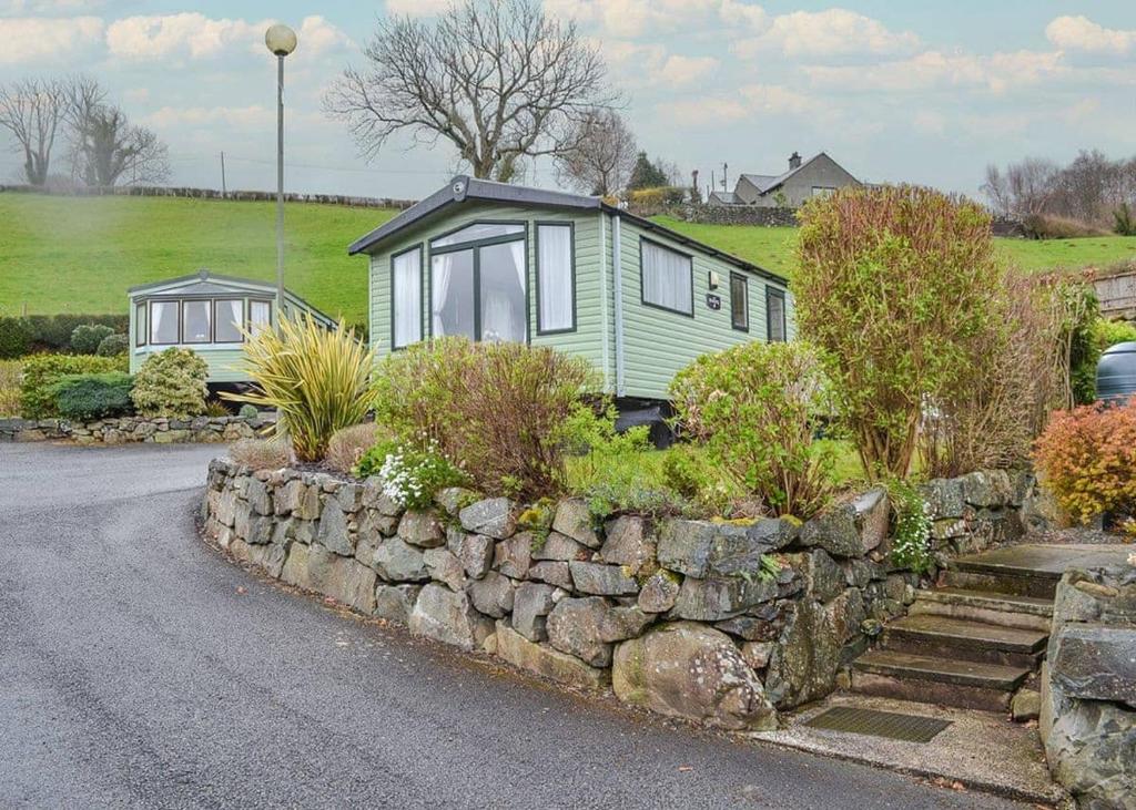 a green caravan parked next to a stone wall at Tan-y-fron Holiday Park in Dolgellau