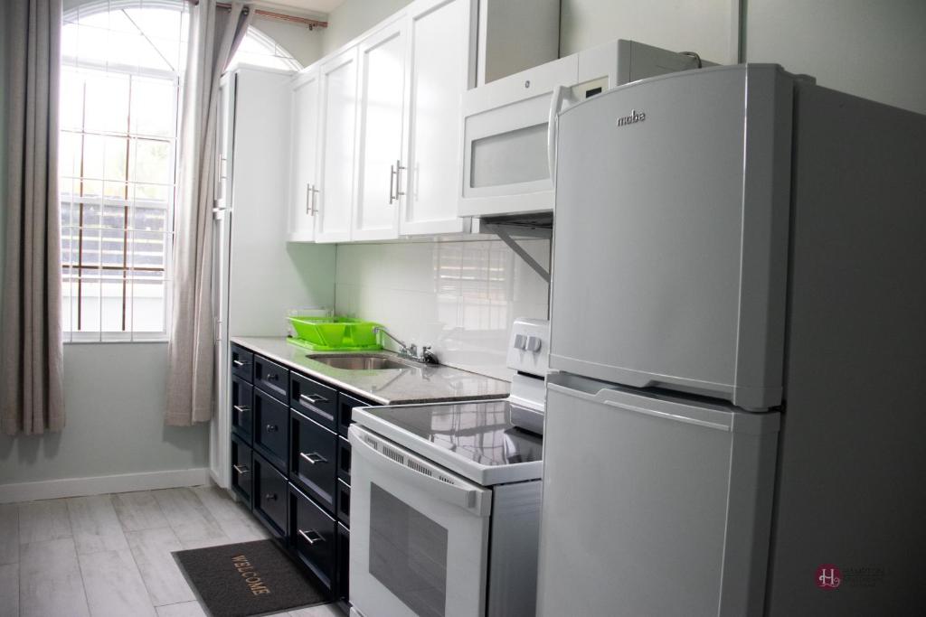 a kitchen with white cabinets and a refrigerator at Hampton Apartments Guyana in Georgetown