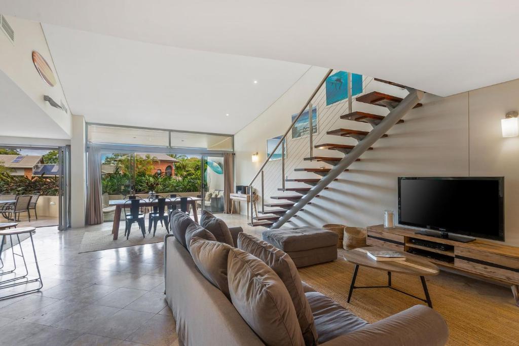 a living room with a couch and a tv and a staircase at Jades on Lawson 2 in Byron Bay